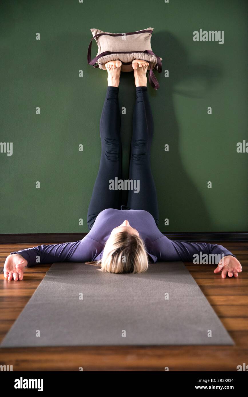 Junge Frau im Yoga, entspannte Pose mit Beinen an der Wand mit schweren Sandsäcken Stockfoto