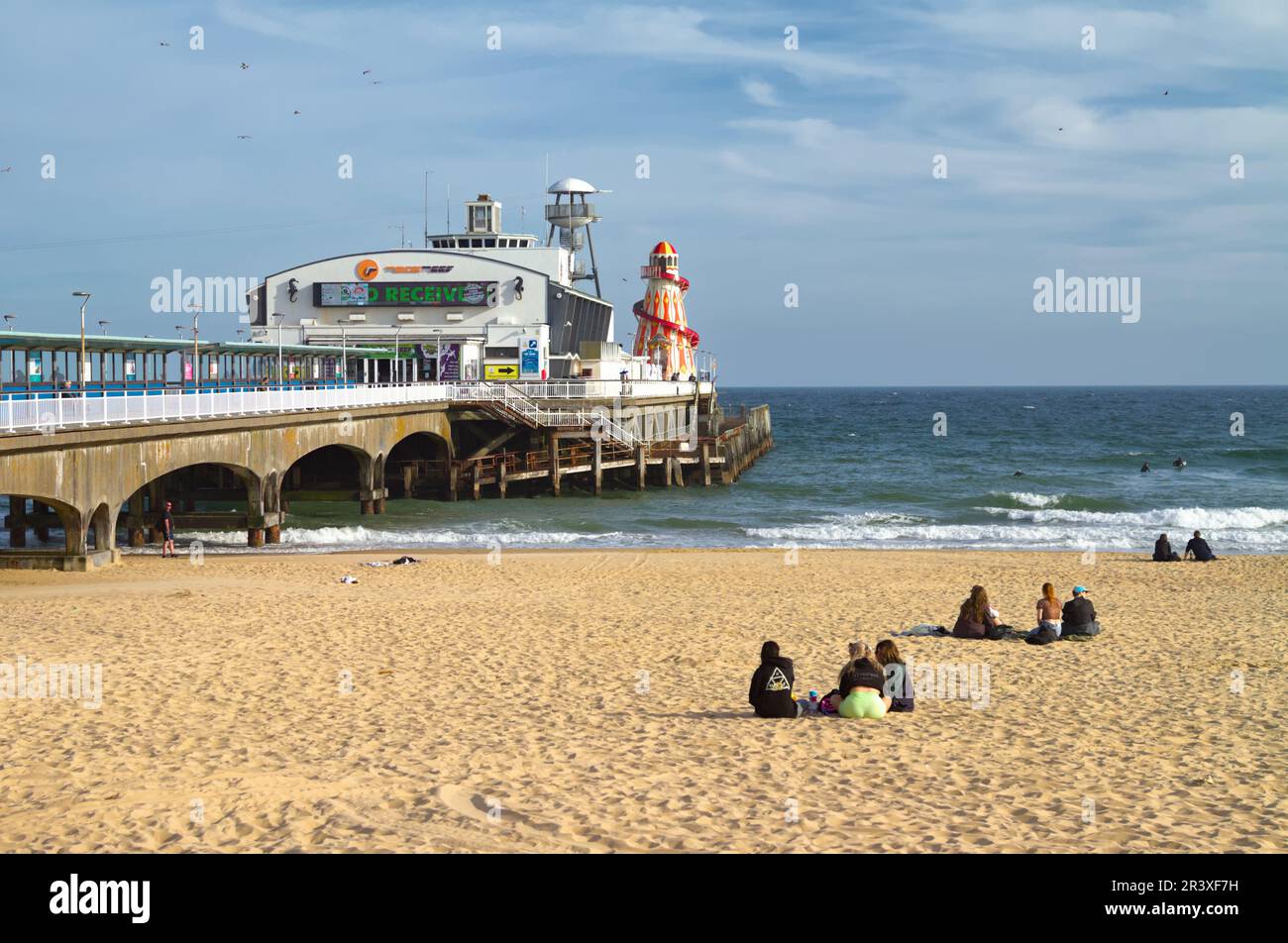 Leute, die an Einem Frühlingstag am Bournemouth Beach sitzen, mit Bournemouth Pier, England, Großbritannien Stockfoto