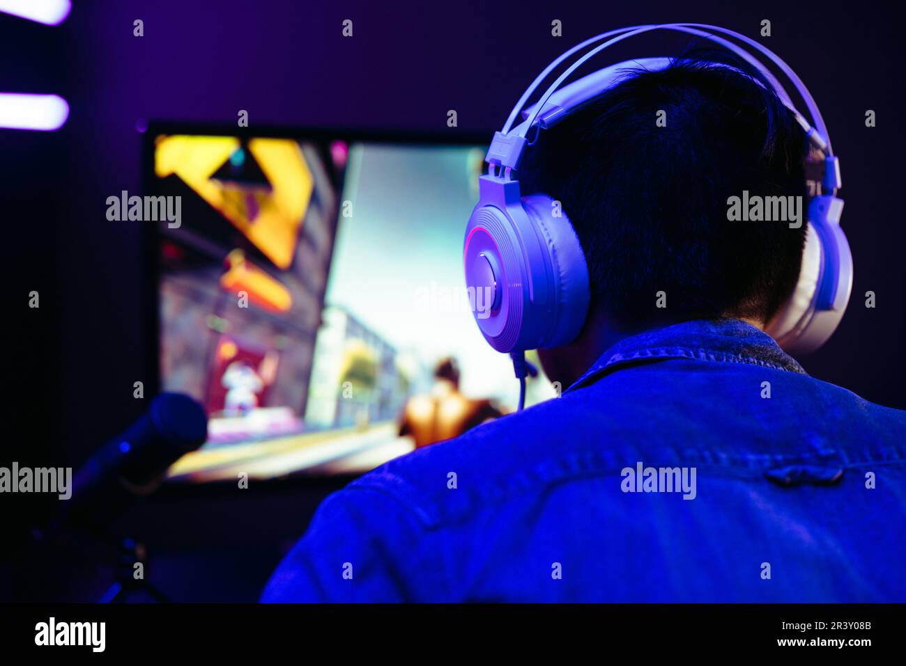 Männlicher Streamer, der sich mit aufgesetzten Kopfhörern in seinen Gaming-Computer eingewöhnt. Computerspieler, der in der Online-Multiplayer-Welt des Ego-Shots navigiert Stockfoto