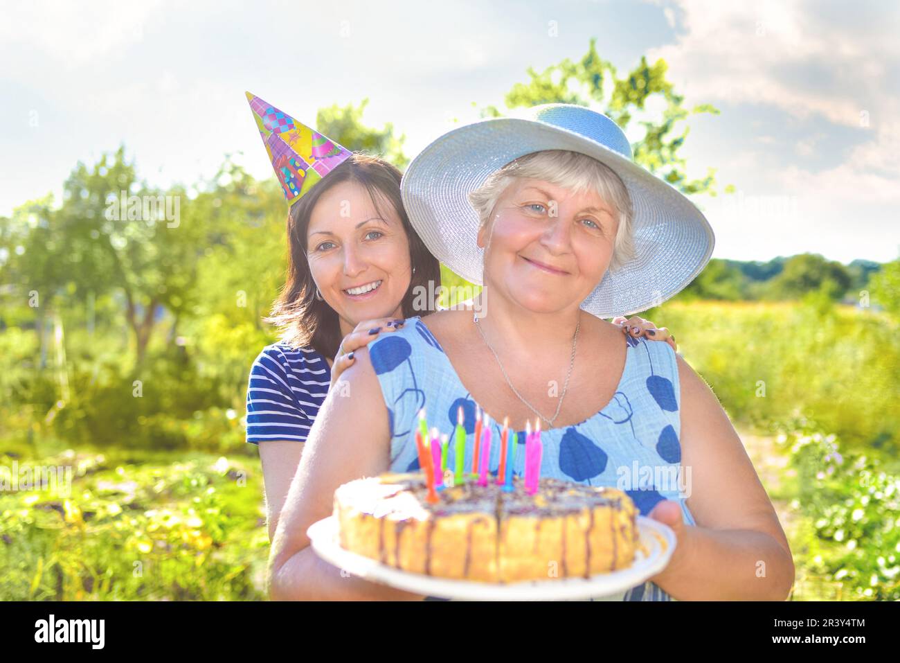 Großmutter Geburtstag, die mit einem Lächeln, zusammen mit ihrer Tochter im Dorf und hält einen Geburtstag hausgemachten Kuchen. Stockfoto