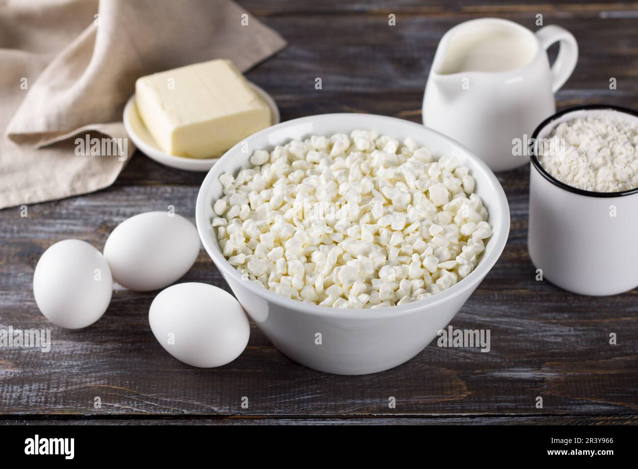 Schüssel mit Hüttenkäse, Eiern, Mehl, Butter, Milch auf Holzhintergrund Stockfoto
