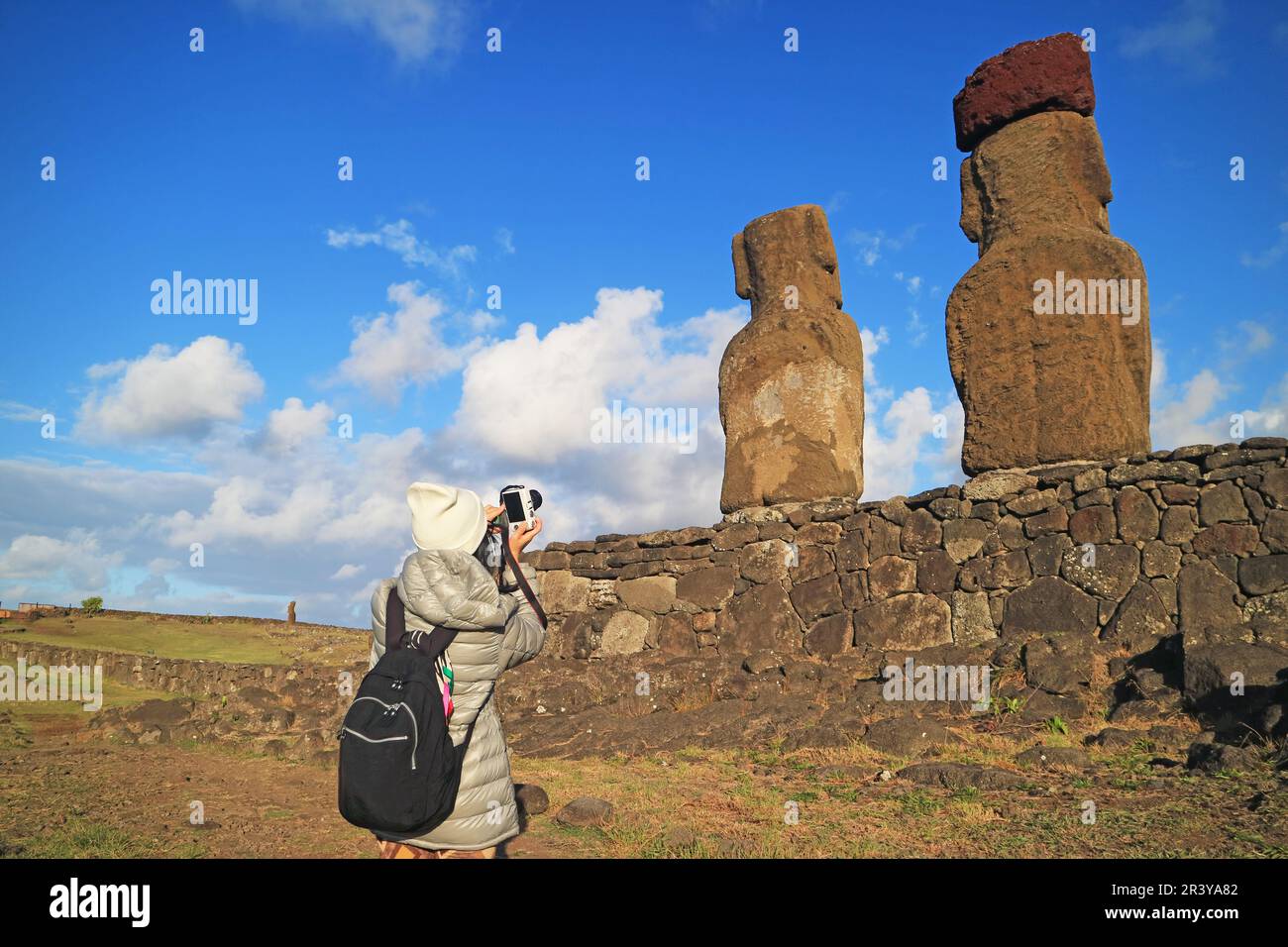 Weibliche Reisende, die auf der Rückseite gigantischer Moai-Statuen auf ...