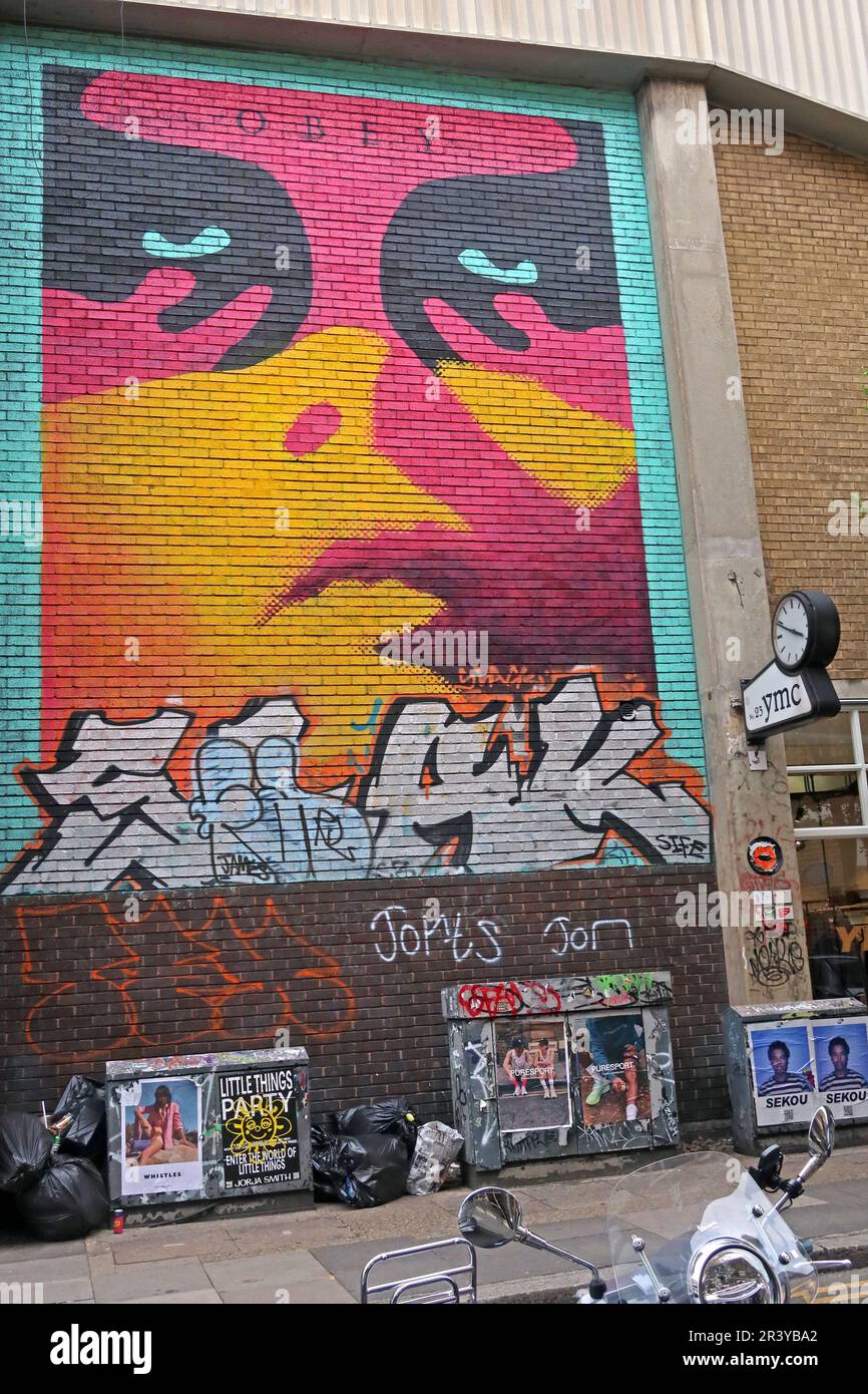 Obey Street Art Wandgemälde von Shepard Fairey an einer Backsteinmauer an der Hanbury Street in Spitalfields, East London, umgeben von Graffitis und Plakaten Stockfoto