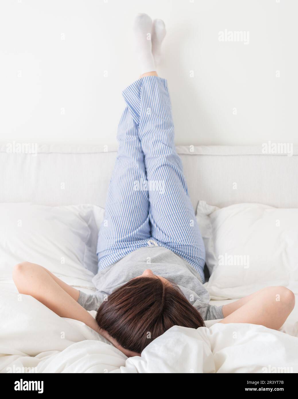 Die Beine der Frau waren hoch und die Arme unter ihrem Kopf lagen im Bett und trugen einen Pyjama Stockfoto