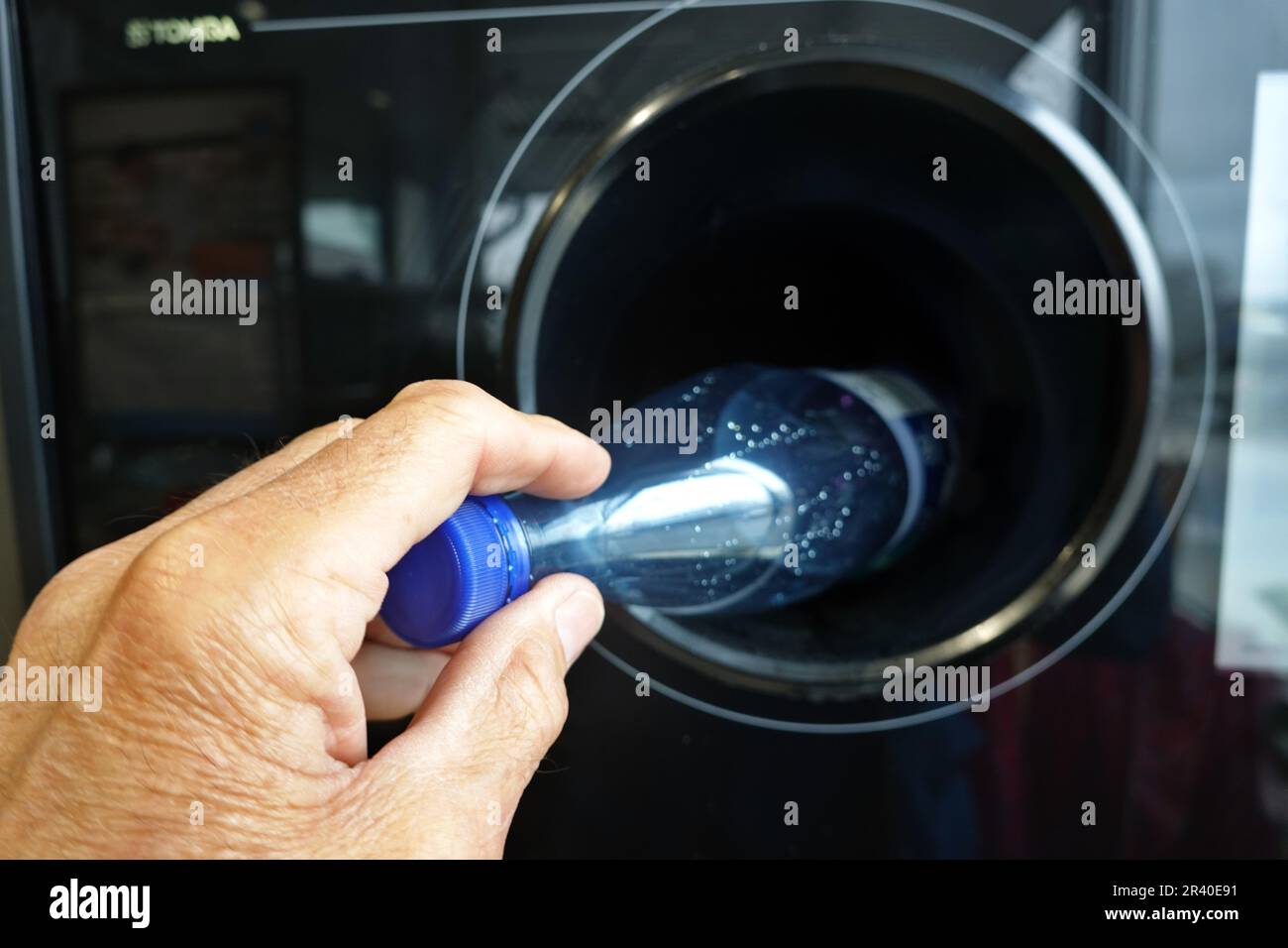 Symbolische Bilderrückgabemaschine für PET-Ablagerungsflaschen – die Hand eines Mannes wirft eine PET-Flasche in eine Maschine Stockfoto