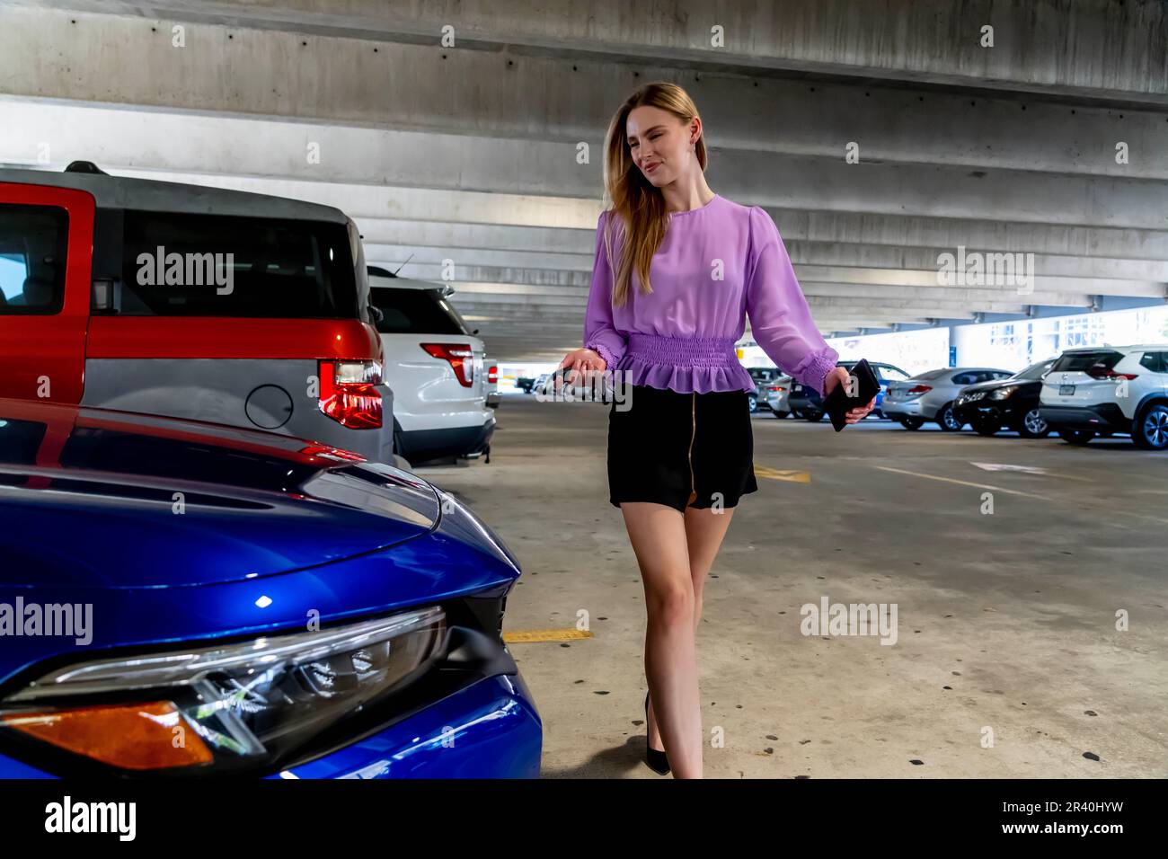 Eine hübsche blonde Assistentin geht nach Einem langen Tag auf Einem überdachten Parkplatz zu ihrem Auto Stockfoto