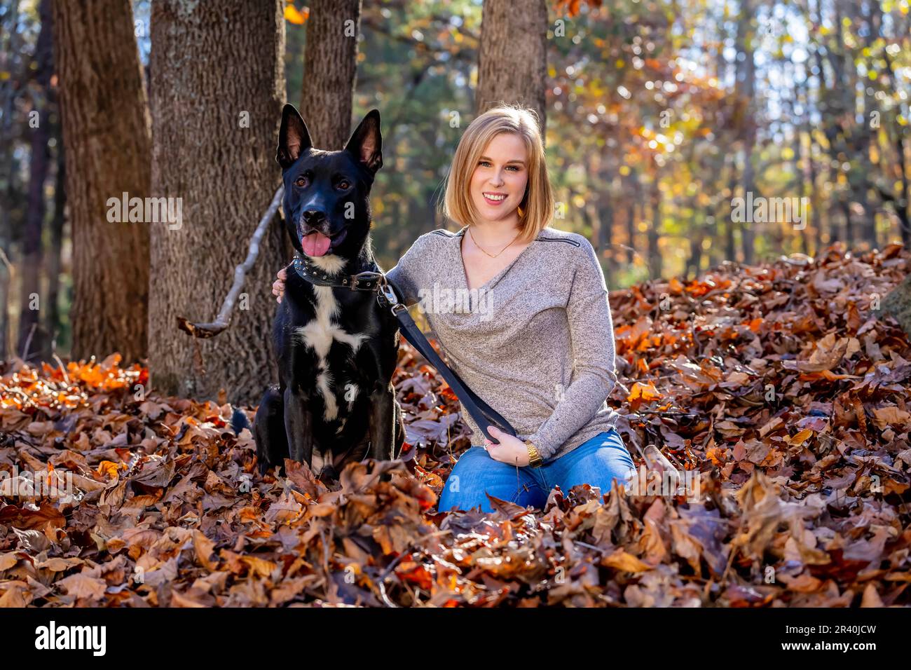 Ein hübsches blondes Model steht draußen und genießt das Herbstwetter mit ihrem Hund in Einem Park Stockfoto