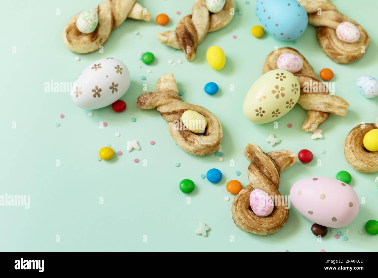 Färbt Ostereier mit Kaninchenbrötchen in Osterform mit Zimt auf pastellgrünem Hintergrund. Frohe Osterferien. Stockfoto