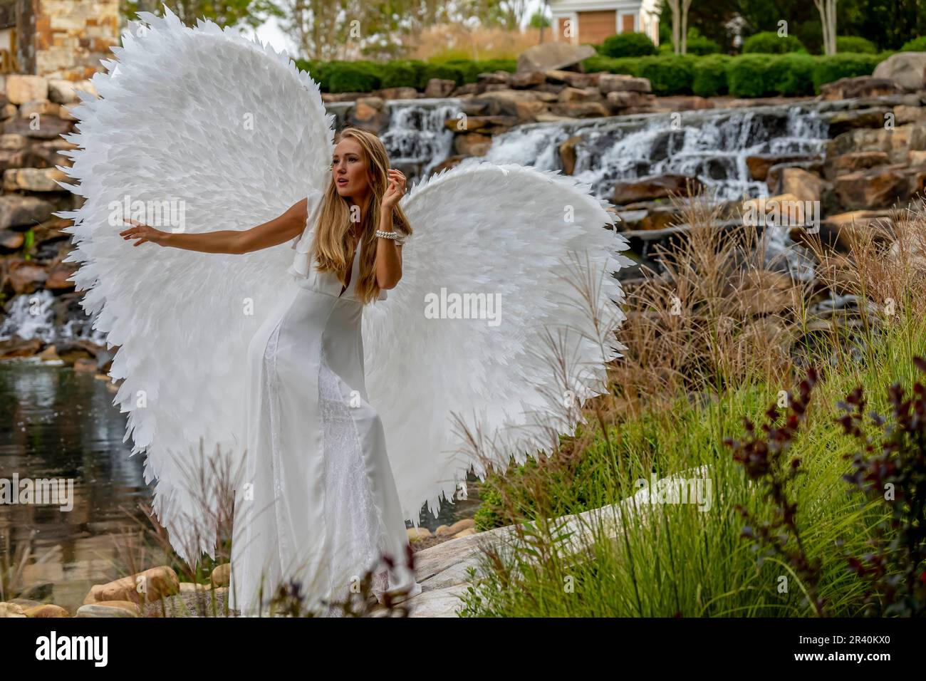 Ein hübsches blondes Model posiert draußen und trägt weiße handgefertigte Flügel zu Halloween Stockfoto