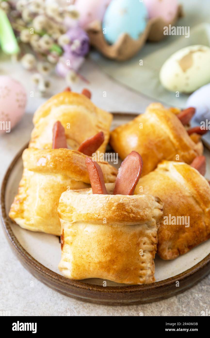 Brötchen in Form eines Osterkaninchens aus Wurst und Käse in einem Hefeteig mit gefärbten Eiern auf grauem Steinhintergrund. Trad Stockfoto