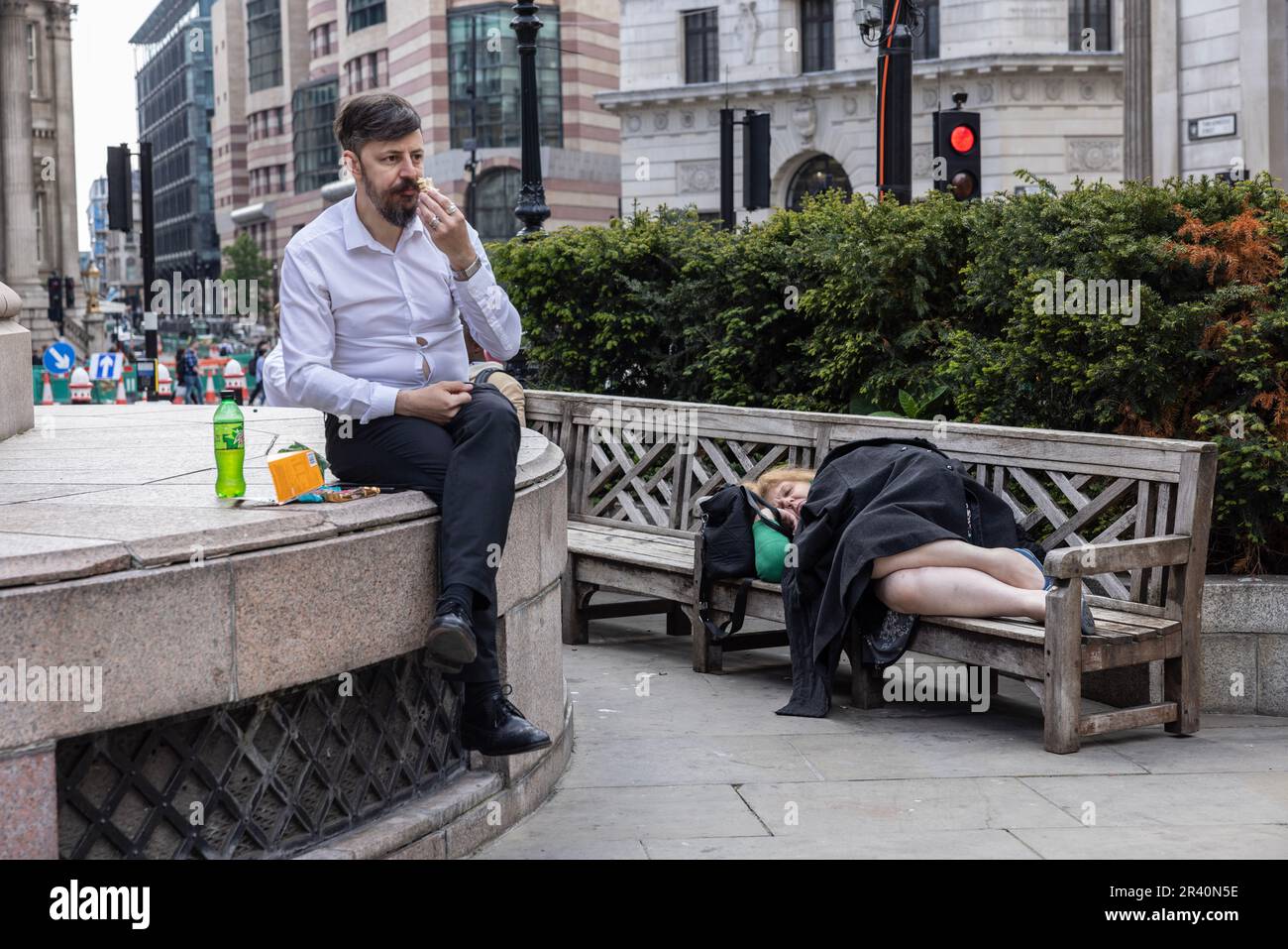 Stadtarbeiter isst sein Mittagessen, während eine Frau auf einer Bank in der Nähe der Royal Exchange, City of London, England, Großbritannien, schläft Stockfoto