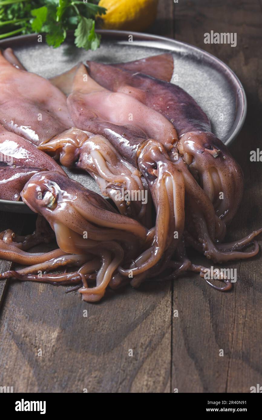 Rohe Kalmare auf grauen Platten mit Koriander und Zitronen. Auf dunklem Holzhintergrund. Stockfoto