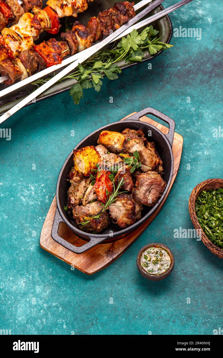 Grillfleisch - Schweinefleisch, Huhn und Gemüse auf einer gusseisernen Pfanne. Gegrillte Spieße auf blauem Holzhintergrund. Draufsicht Stockfoto