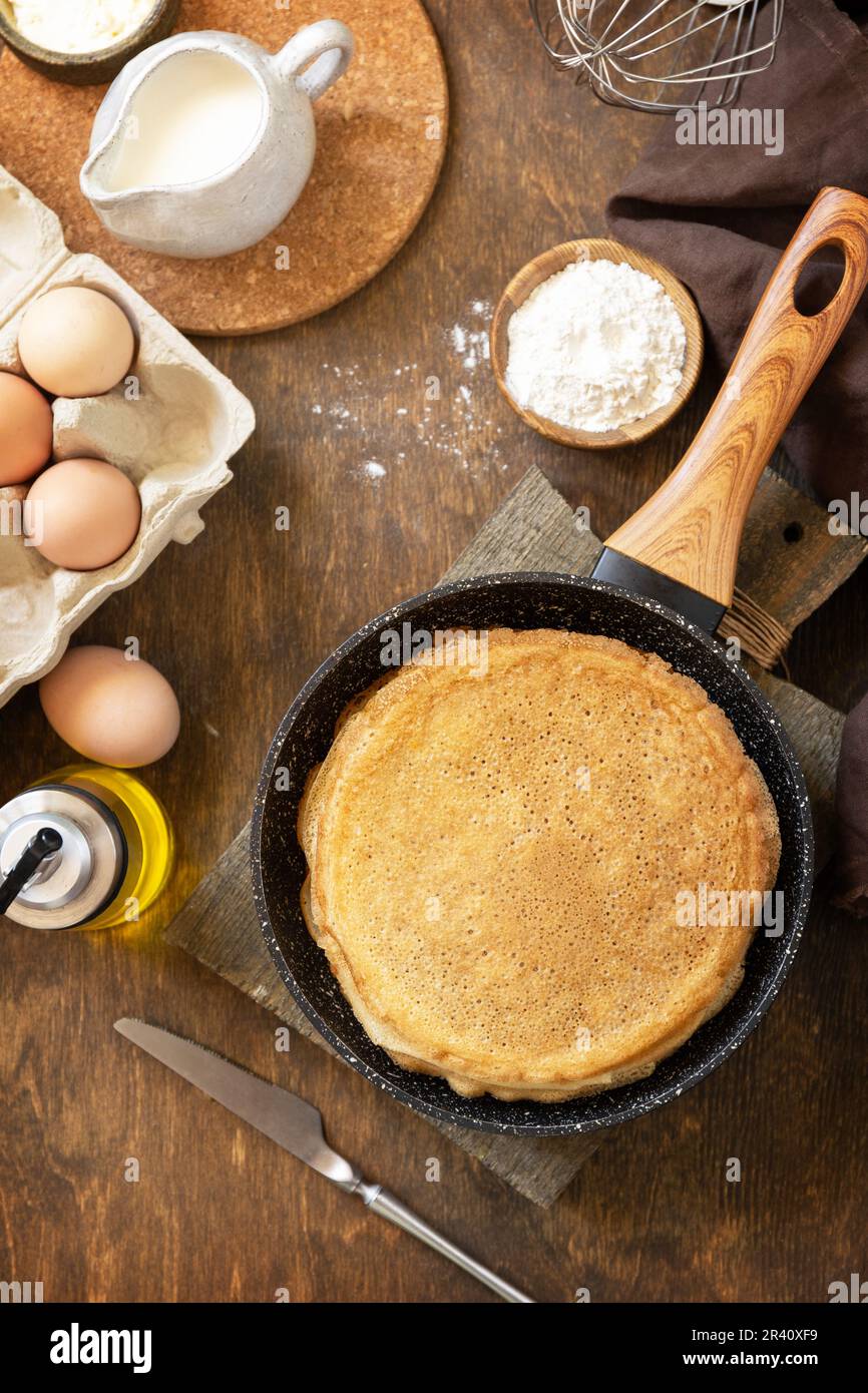 Wir feiern den Pfannkuchen-Tag, kochen ein gesundes Frühstück. Köstliche hausgemachte Crepes oder Pfannkuchen in einer Pfanne und Zutaten auf einem Stockfoto