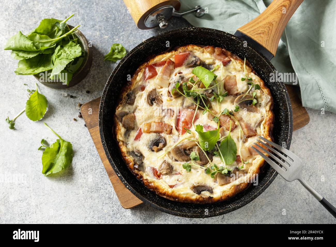 Italienisches Frühstücksgericht. Rustikales Omelett (Frittata) mit Pilzen und Speck auf einer gusseisernen Pfanne. Blick von oben. Stockfoto