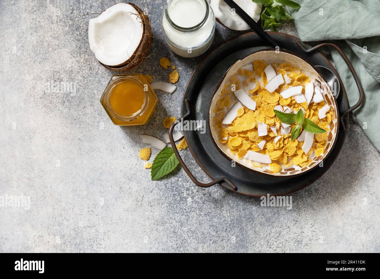 Veganes Sommerfrühstück. Frühstücksflocken aus Müsli und Cornflakes mit alternativer Kokosnussmilch und frischen Kokosnussscheiben auf einem St. Stockfoto