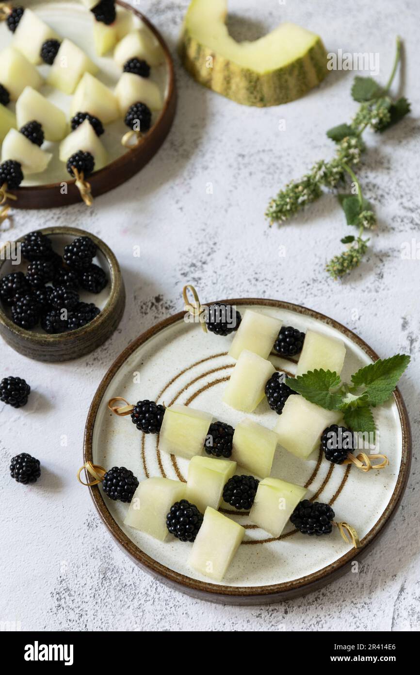 Festlicher Sommersnack mit Obst und Beerencanapés. Veganes Essen. Kanapees mit Melone und Brombeeren auf einem Steintisch. Speicherplatz kopieren Stockfoto