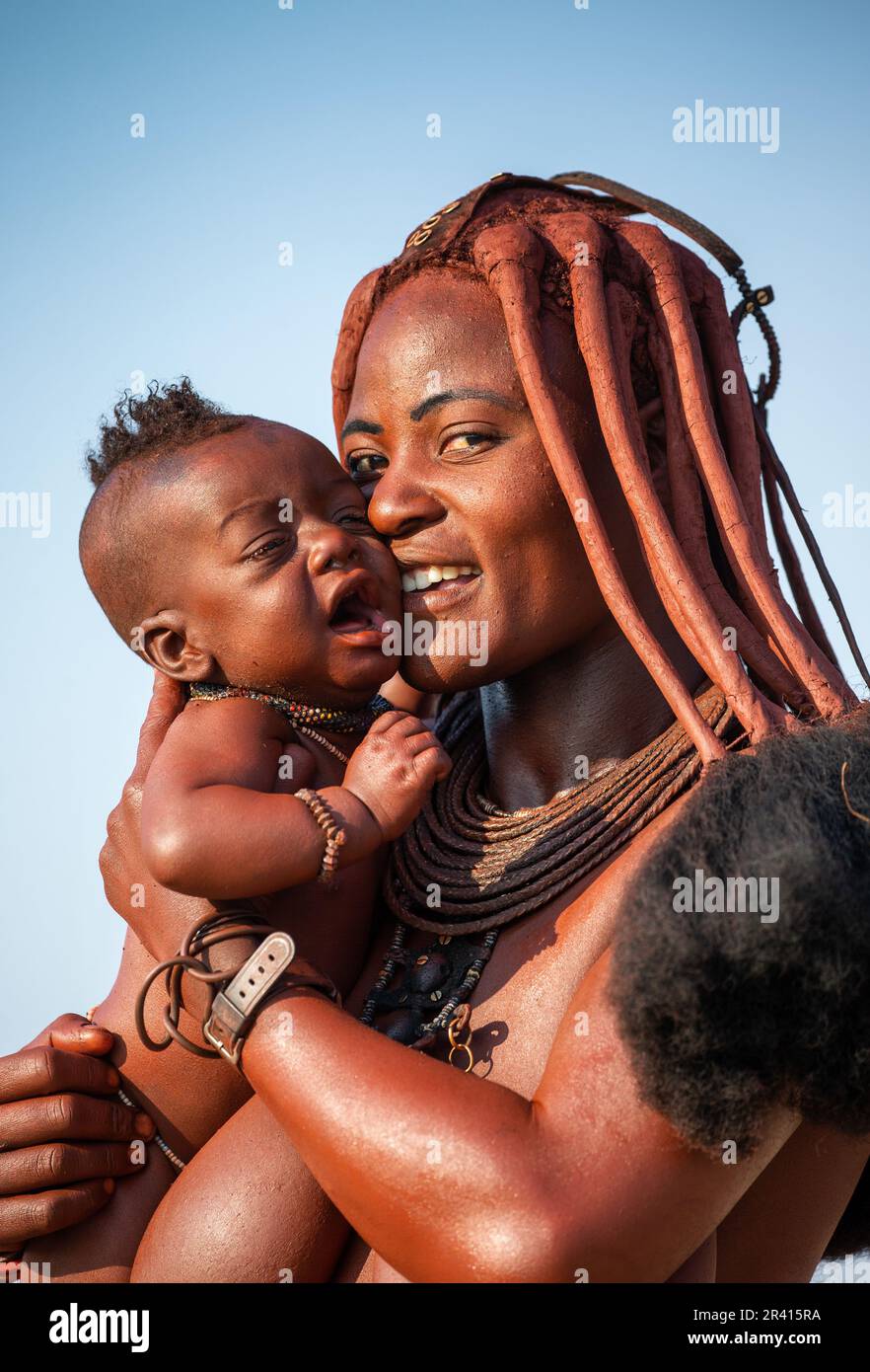 Porträt einer jungen Frau des Himba-Stammes mit einem kleinen Kind in ihren Armen. Stockfoto
