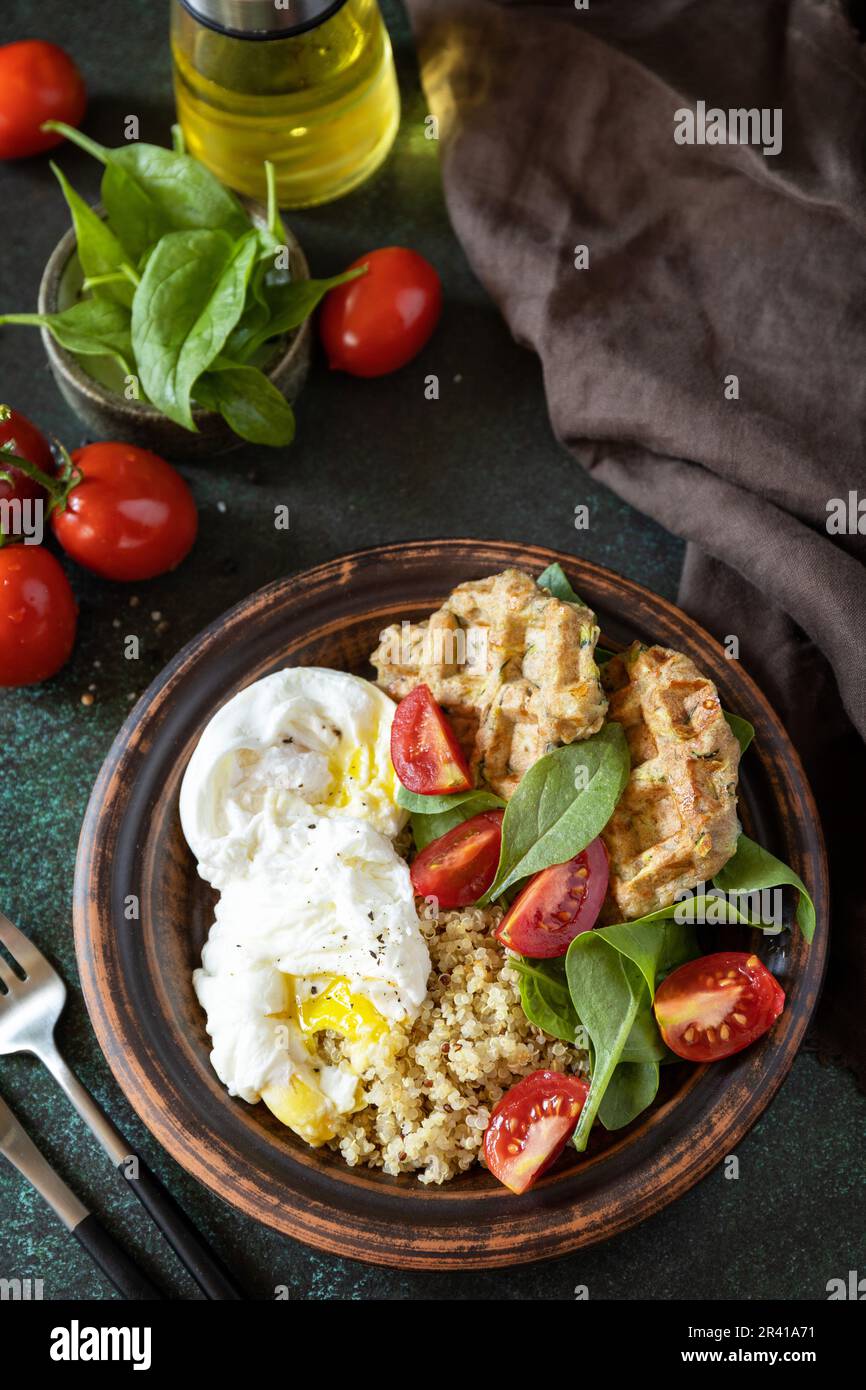 Vegane Zucchini-Waffeln, pochiertes Ei, Quinoa und frischer Gemüsesalat auf einem Steintisch. Keto-Diät. Köstliches Frühstück oder bru Stockfoto