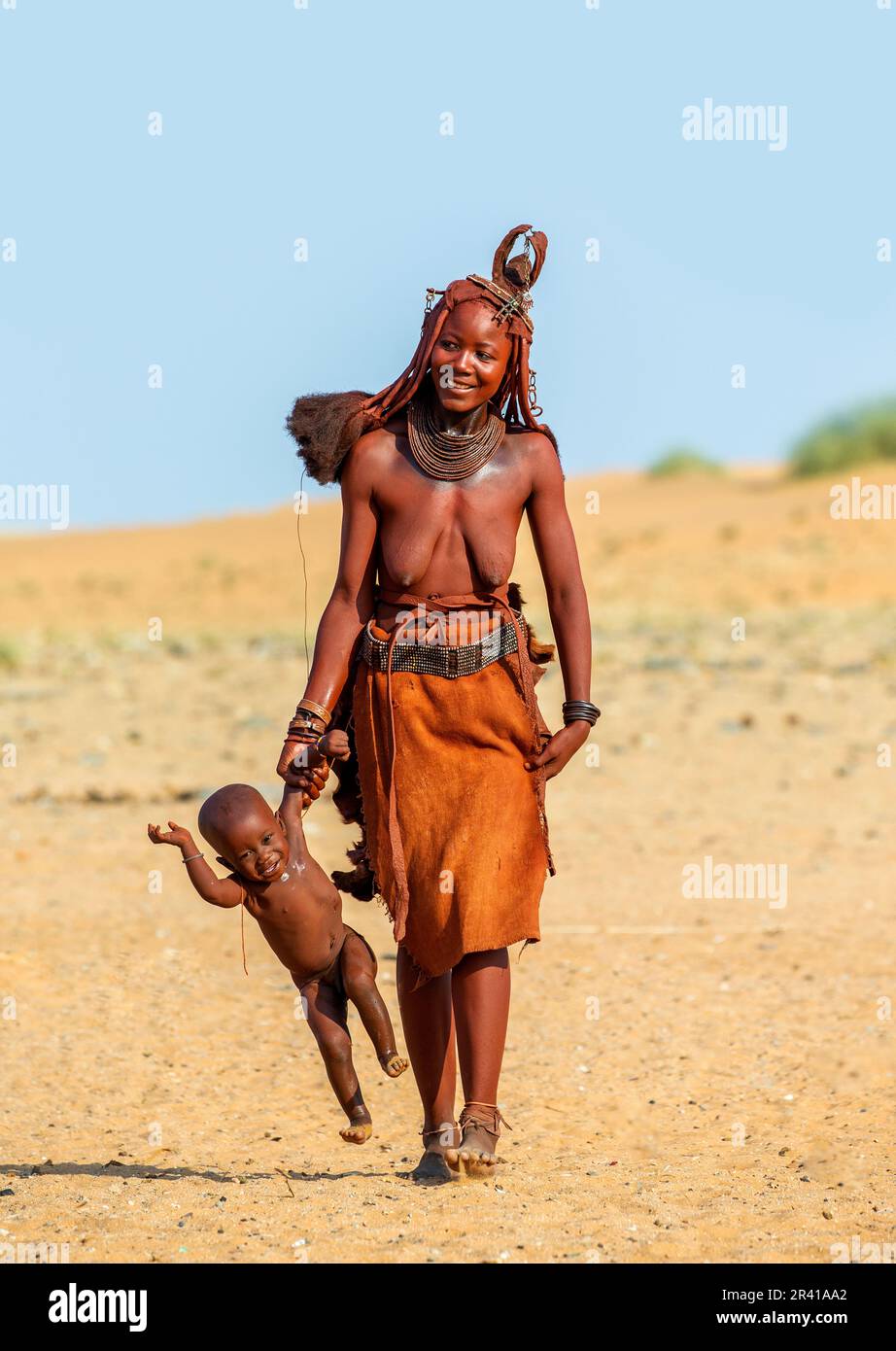 Himba-Frau trägt ihr Kind und hält seine Hand. Stockfoto