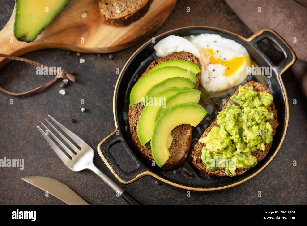 Vollkornbrot, Avocado in Scheiben und pochiertes Ei auf Steinhintergrund. Gesundes Frühstückskonzept, Sandwich mit Avocado und Stockfoto