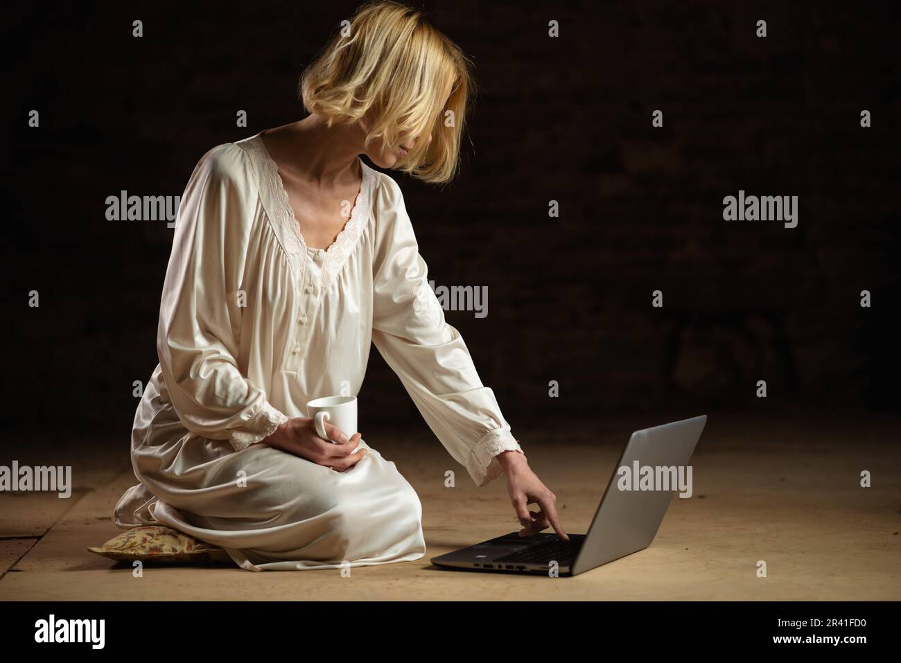 Eine unbekannte Frau in einem leeren Raum mit Kaffee in der Hand und einem Notebook auf dunklem Hintergrund. Frist, Recyclingkonzept. Eine Frau mittleren Alters Stockfoto