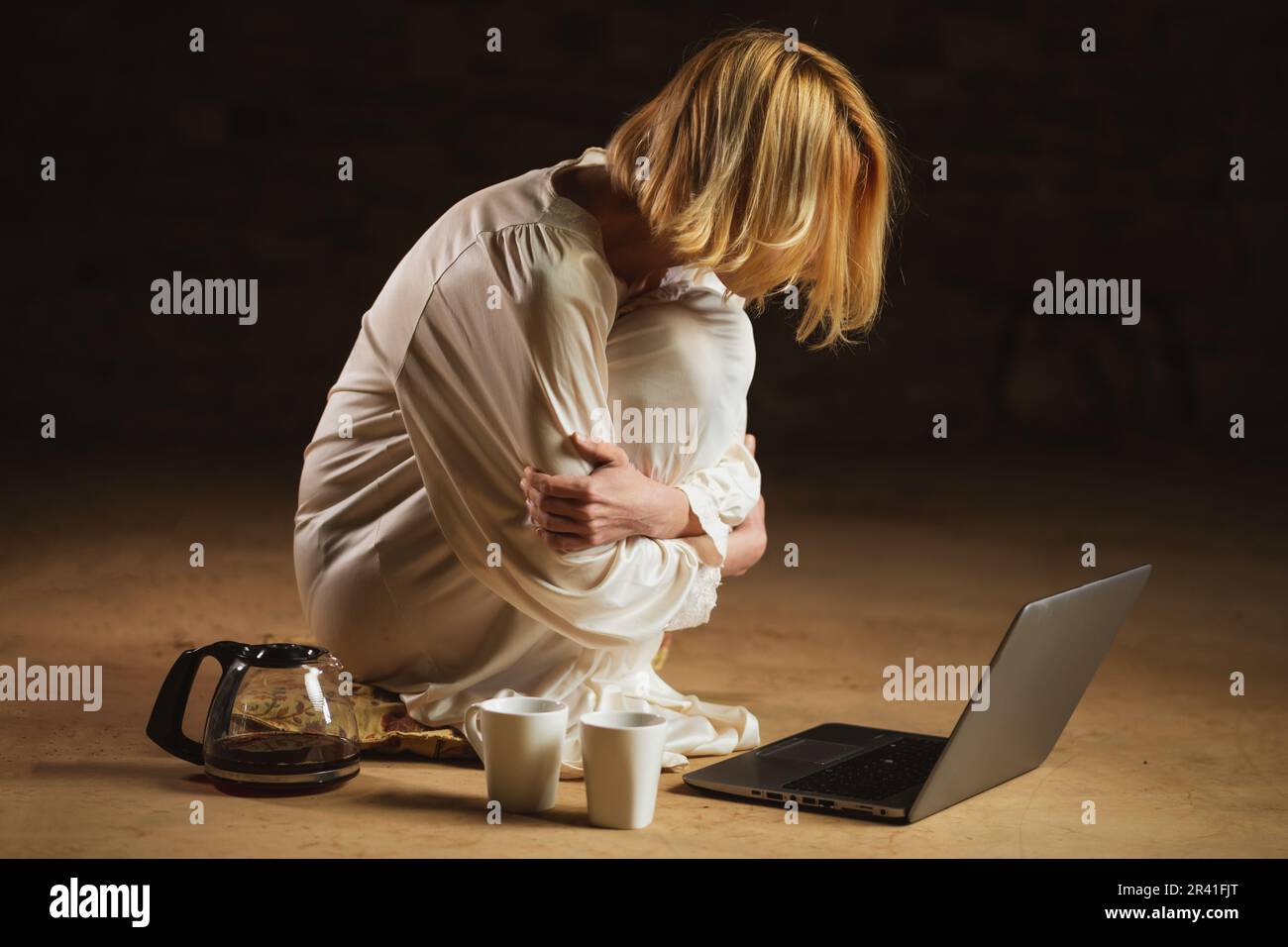 Frau mit Kaffeetasse vor dem Laptop. Leerer Raum, dunkler Hintergrund. Deadline, Recycling, Fleiß-Freelancer-Konzept. Stockfoto