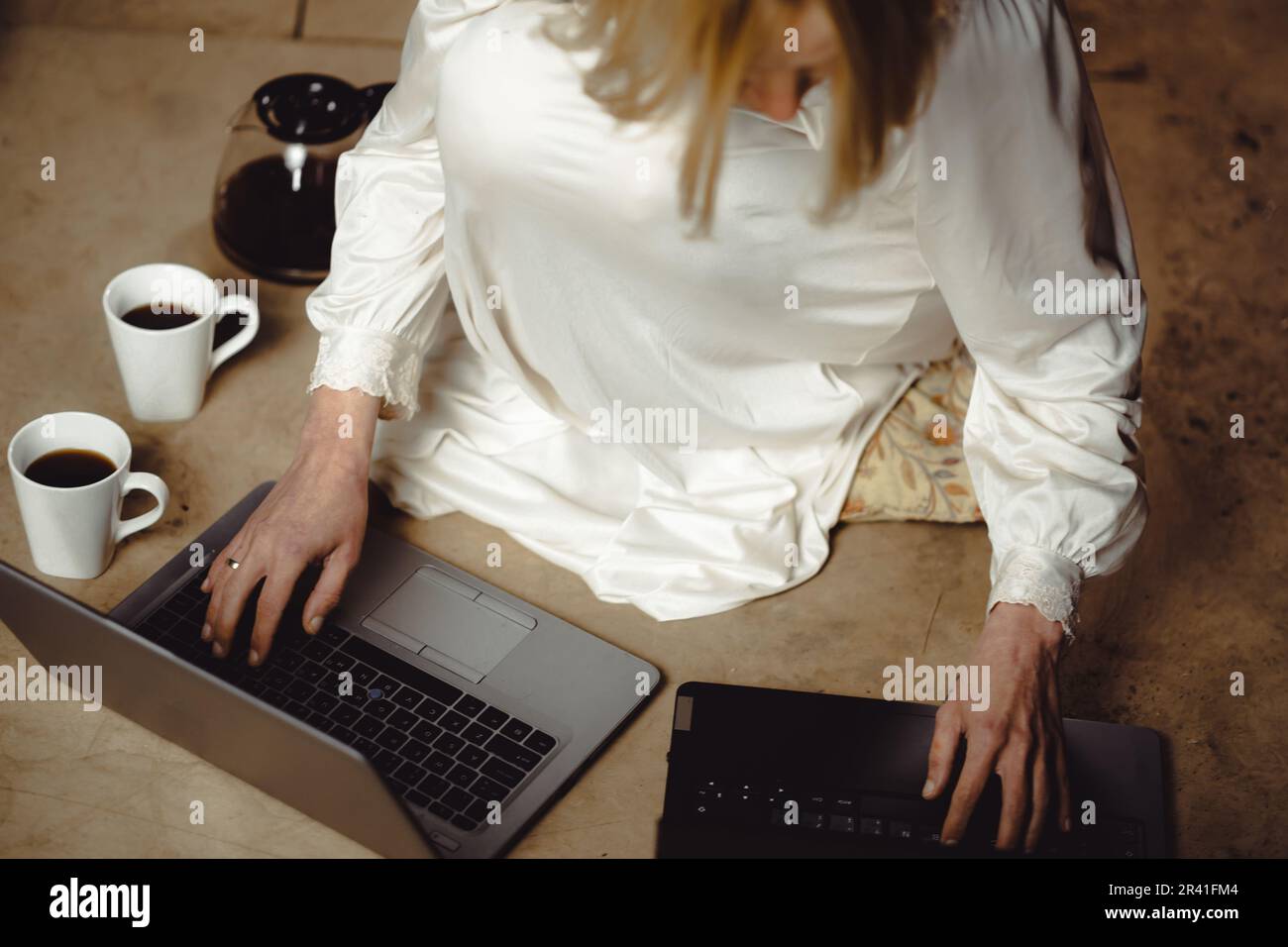 Frau mit Kaffeetassen vor zwei Laptops. Deadline, Nacharbeit, Multitasking, Fleiß-Freelancer-Konzept. Stockfoto