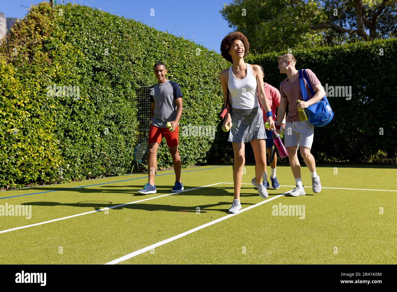 Glückliche, vielfältige Gruppe von Freunden, die zusammen auf dem Tennisplatz ankommen Stockfoto