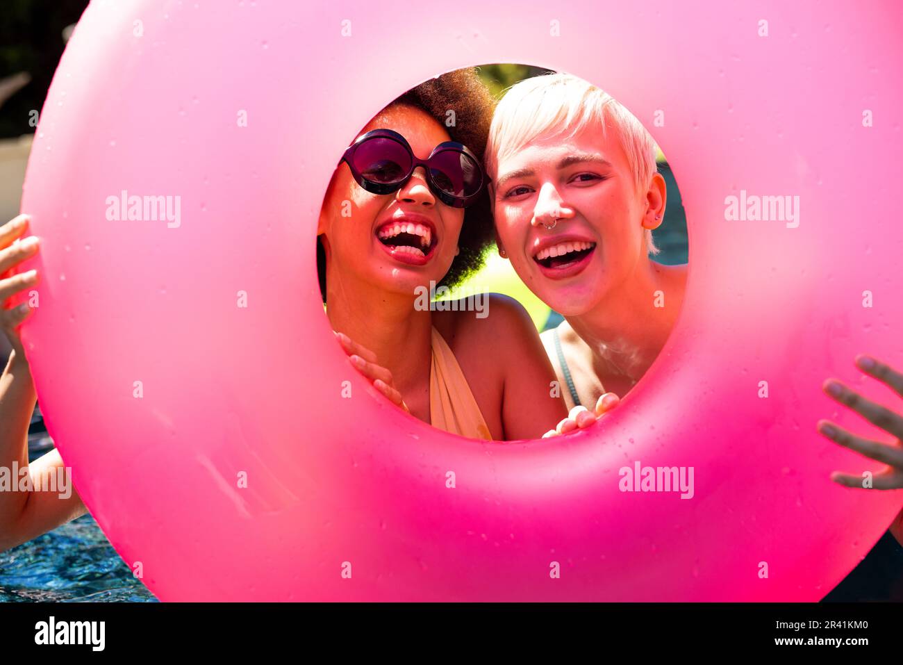 Porträt von fröhlichen, vielfältigen Freundinnen, die eine Poolparty veranstalten, einen Schwimmring halten und im Garten lächeln Stockfoto