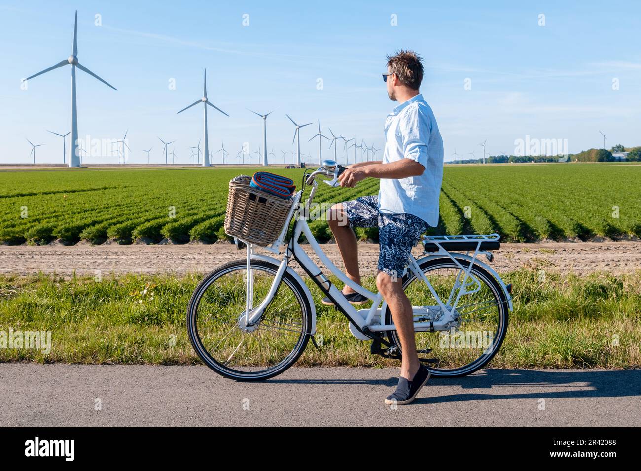 Junger Mann, elektrisches grünes Fahrrad bei einer Windmühlen Farm, Windmühlen isoliert in einem wunderschönen Sommer Stockfoto