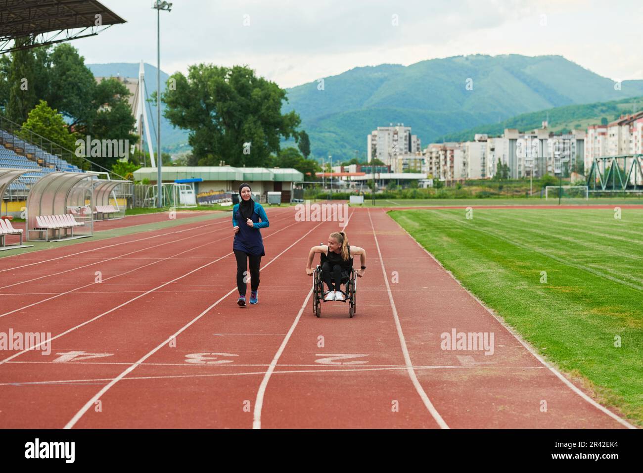 Eine muslimische Frau in einer Burka, die zusammen mit einer Frau im Rollstuhl auf dem Marathonkurs läuft, um sich auf den zukünftigen Wettkampf vorzubereiten Stockfoto