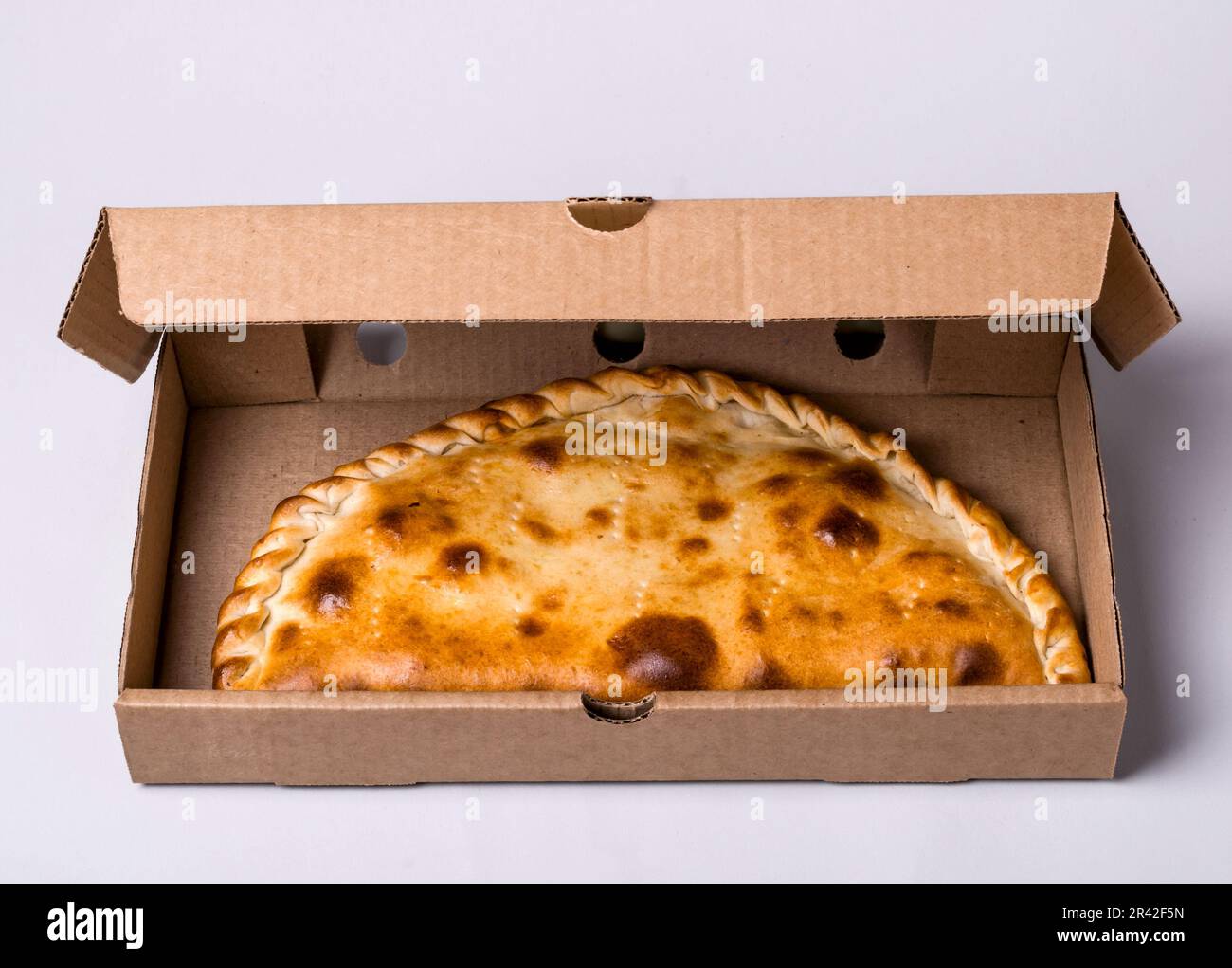 Geschlossene Pizza-Calzone in Packbox auf grauem Hintergrund Stockfoto