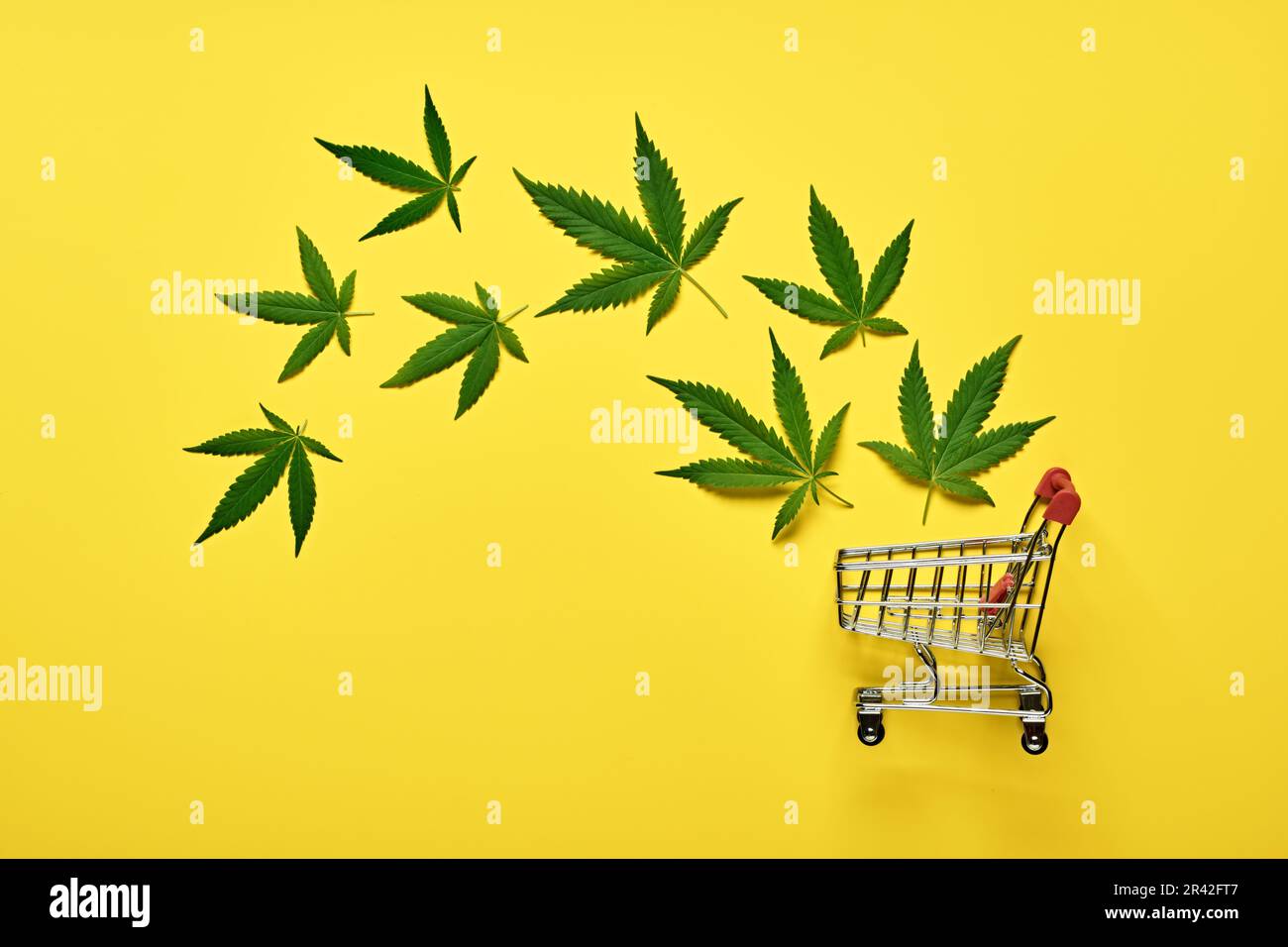 Einkaufswagen und Marihuana-Blätter auf gelbem Hintergrund. Legales Cannabiskonzept Stockfoto