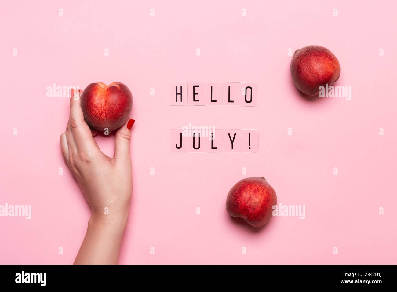 „Hallo Juli“-Text und weibliche Hand mit reifem Pfirsich auf pinkfarbenem Hintergrund. Hallo Juli Concept Stockfoto