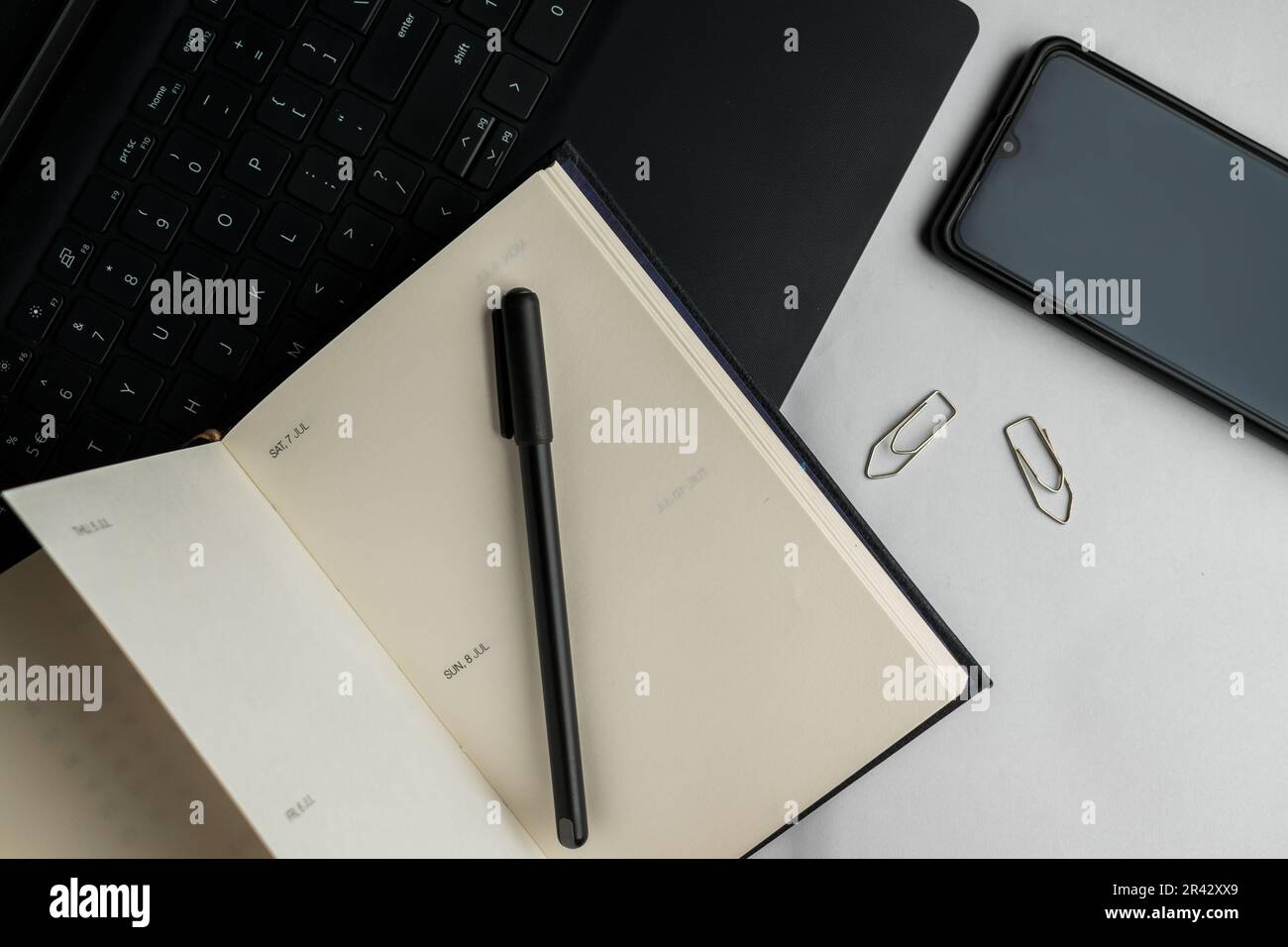 Flach liegender Schreibtisch mit Notebook, Stift, Laptop, Handy und Büroklammern auf weißem Hintergrund. Stockfoto