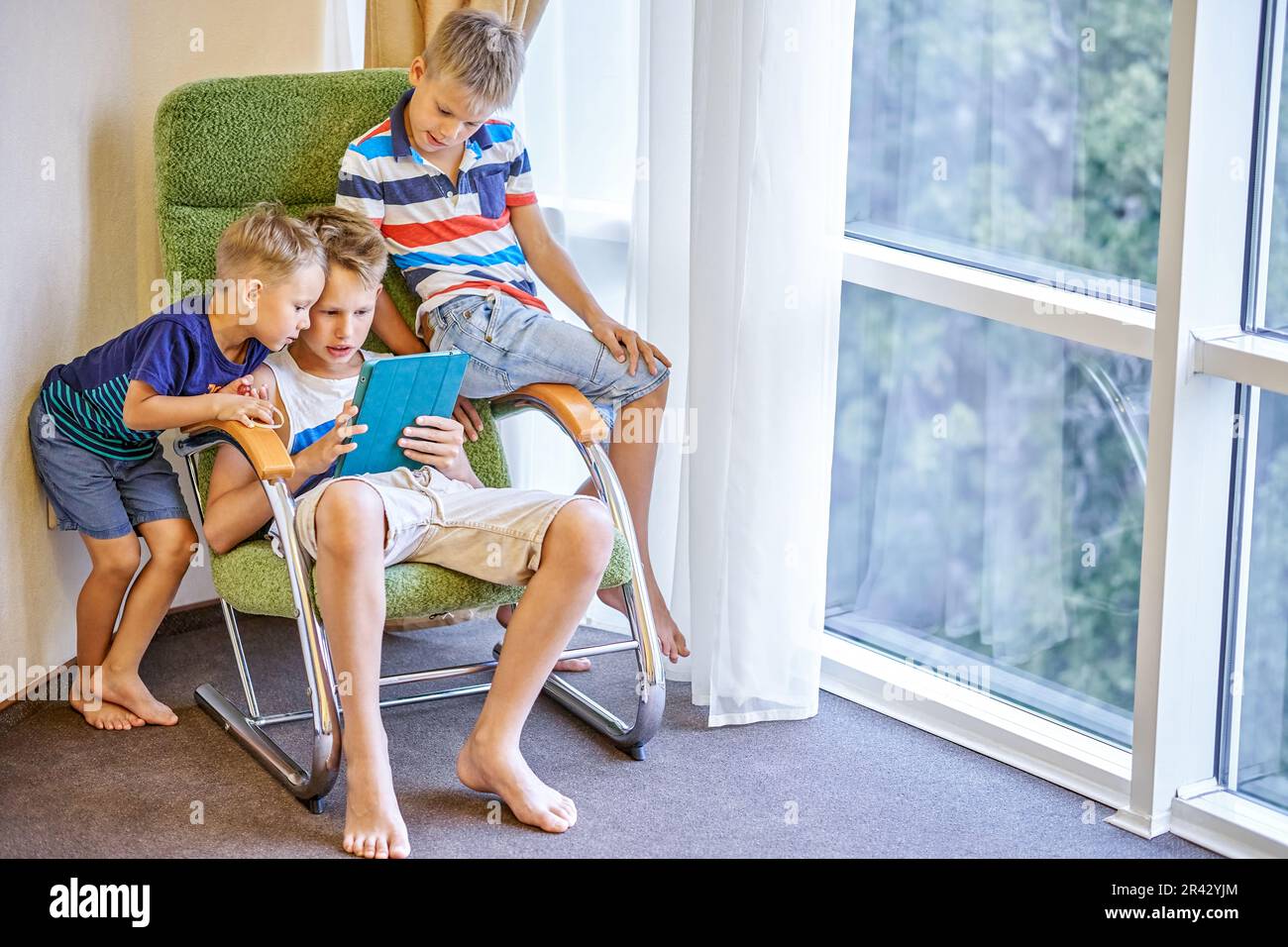 Geschwister von Jungen spielen gemeinsam interessante Spiele auf Tablets. Jüngere Brüder sehen sich im Hotelzimmer einen jungen Schuljungen an, der ein Spiel spielt Stockfoto