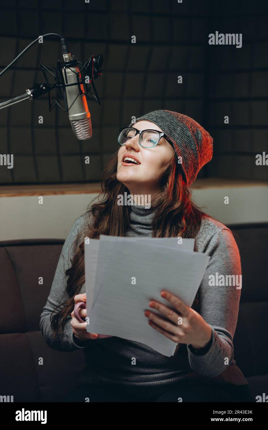 Eine Frau, die vor der Radiosendung Material vorbereitet, Studioaufnahmen. Schalldichter Raum für professionelle Stimmaufnahmen. Der Sprachkünstler arbeitet mit dem Material von so Stockfoto