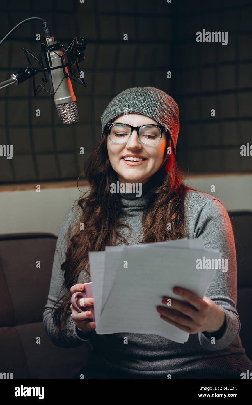 Eine Frau, die vor der Radiosendung Material vorbereitet, Studioaufnahmen. Schalldichter Raum für professionelle Stimmaufnahmen. Der Sprachkünstler arbeitet mit dem Material von so Stockfoto