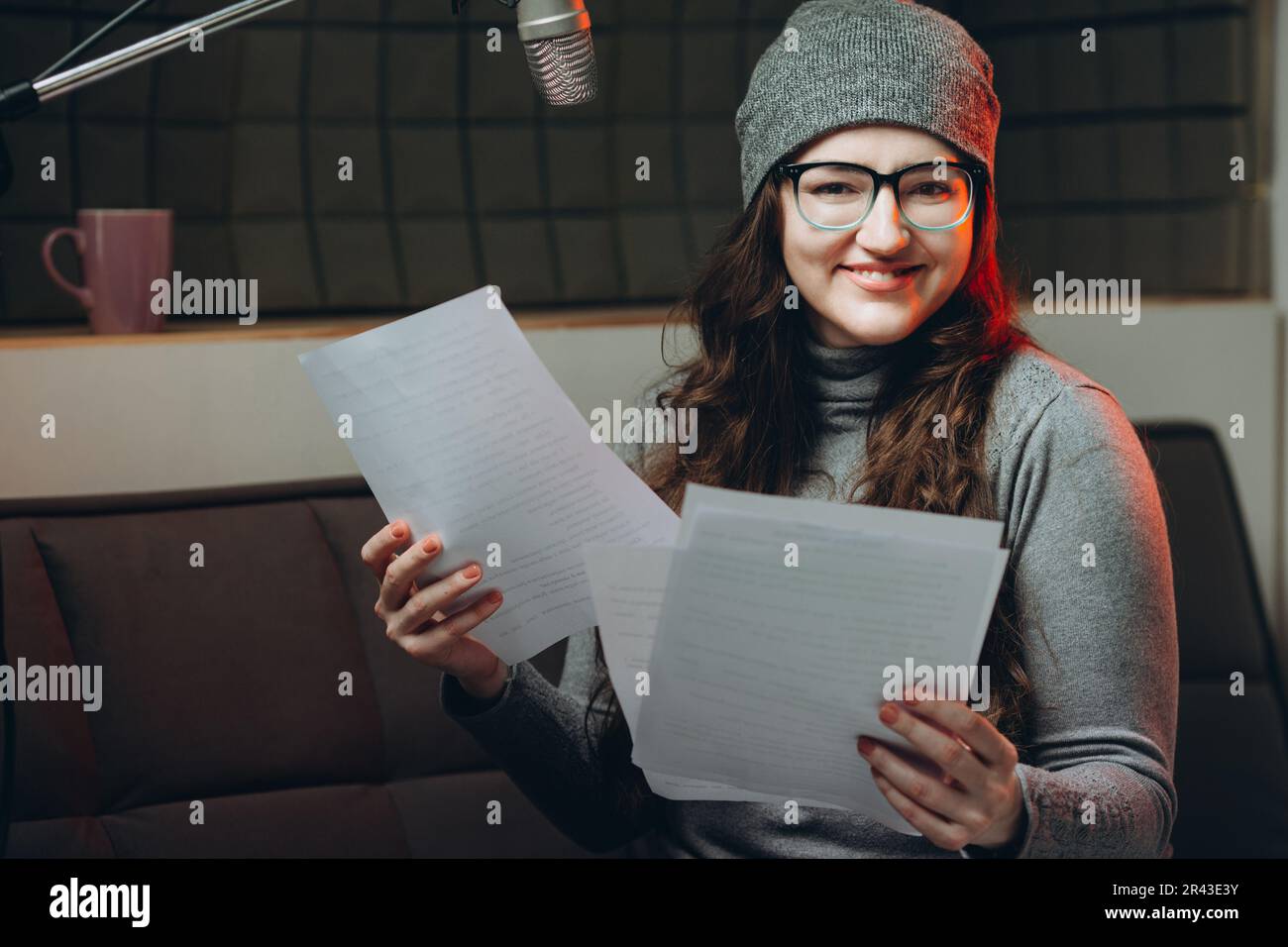 Eine Frau, die vor der Radiosendung Material vorbereitet, Studioaufnahmen. Schalldichter Raum für professionelle Stimmaufnahmen. Der Sprachkünstler arbeitet mit dem Material von so Stockfoto