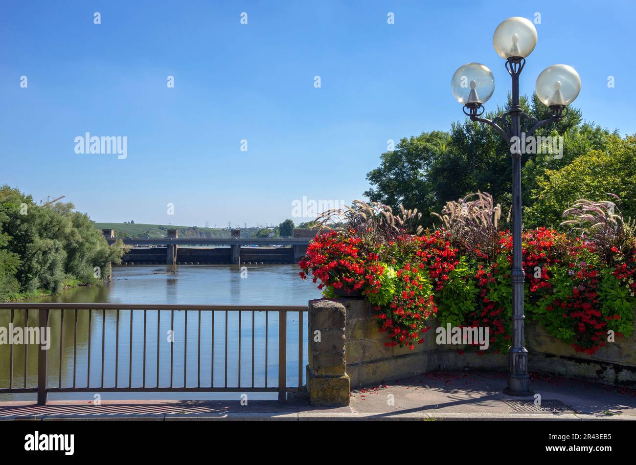 Straßenlaternen und Blumenkästen auf der Neckarbrücke mit Blick auf das Lauffen-Sperrwerk, Baden-Württemberg. Stockfoto