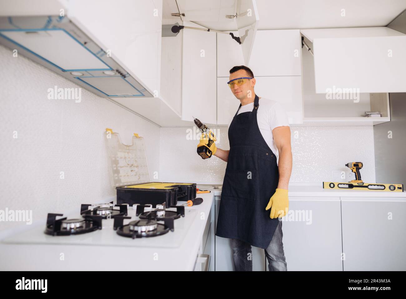 Ein Hausmeister, der Küchenmöbel in einer schwarzen Schürze und gelben Handschuhen mit einem Power-Skrewdriver installiert Stockfoto