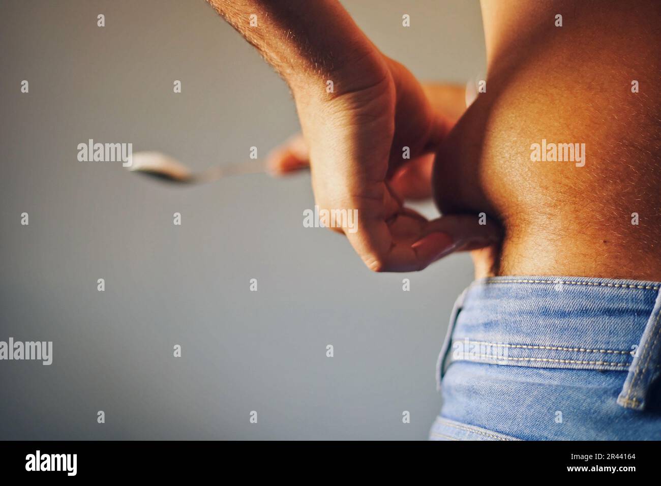 Ein Mann packte seinen Bauch mit einem Zuckerlöffel neben sich. Stockfoto