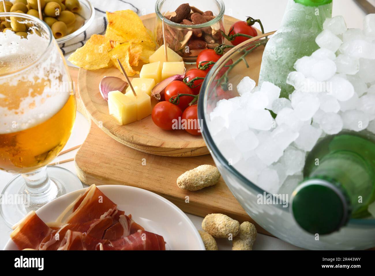 Vorspeise mit kaltem Bier und verschiedenen Fast Food-Gerichten wie Käse, Marmelade, Tomaten, Kartoffeln, Erdnüsse auf weißem Tisch. Erhöhte Aussicht. Stockfoto