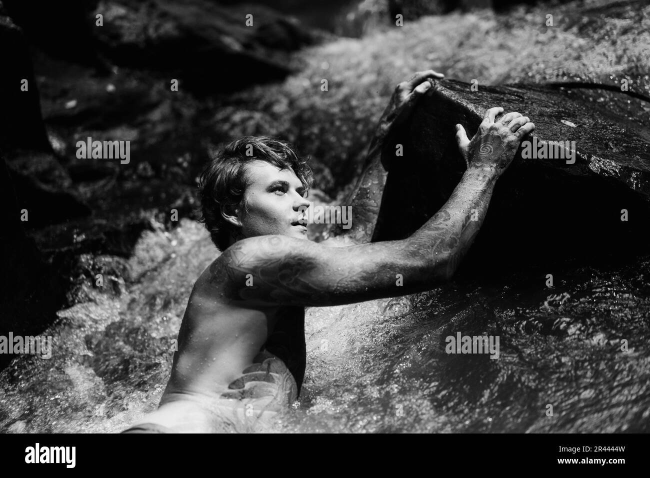 Ein tätowierter junger Mann schwimmt in einem Bergfluss auf Bali. Stockfoto