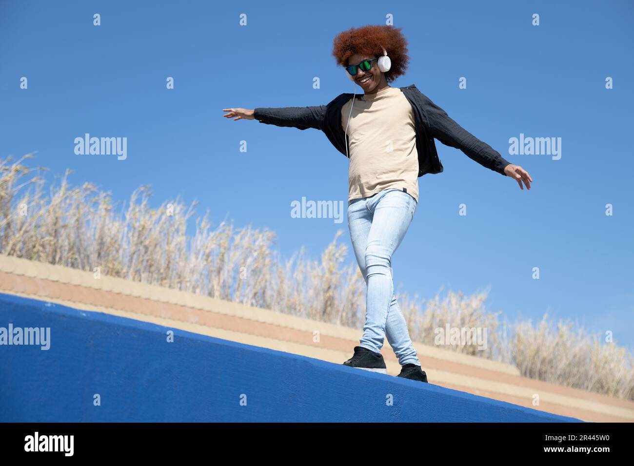 Junger glücklicher Mann mit ausgestreckten Armen balanciert an einer blauen Wand Stockfoto