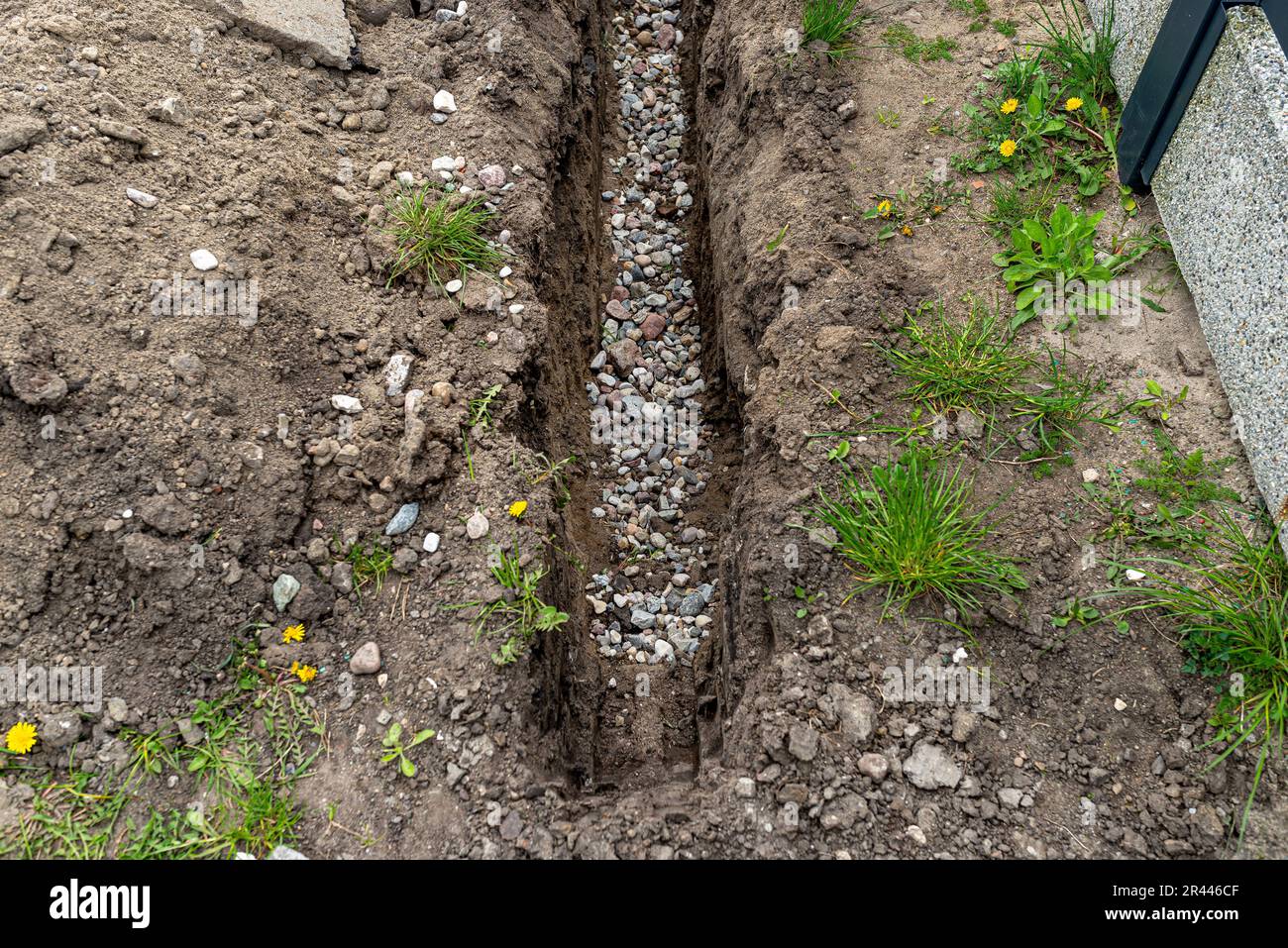 Ein Graben, der im Hof entlang des Zauns gegraben wurde, um das Abflussrohr zu verlegen, sichtbarer Kies. Stockfoto