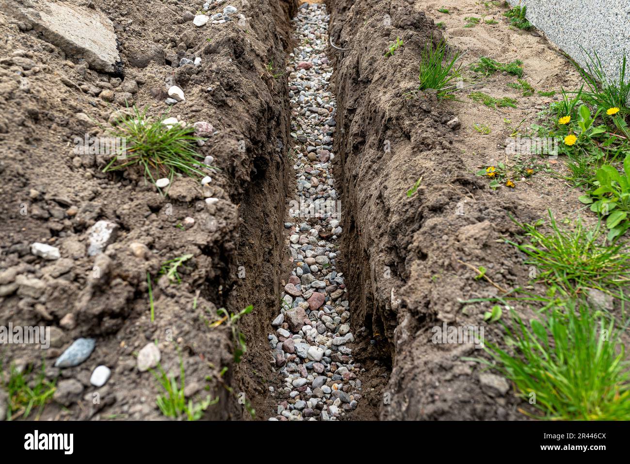 Ein Graben, der im Hof entlang des Zauns gegraben wurde, um das Abflussrohr zu verlegen, sichtbarer Kies. Stockfoto