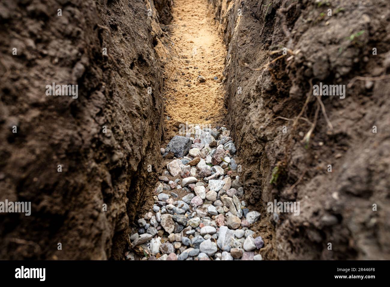 Ein Graben, der im Hof entlang des Zauns gegraben wurde, um das Abflussrohr, sichtbaren Kies und gelben Sand zu verlegen. Stockfoto