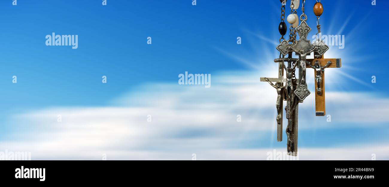 Nahaufnahme einer Gruppe von Metall- und Holzkruzifixen und Rosenkranzperlen vor einem unscharfen, klaren blauen Himmel mit Wolken und Kopierraum. Fotografie. Stockfoto